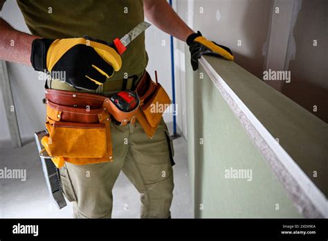 Construction Worker Wearing Tool Belt And Holding Drywall And Utility