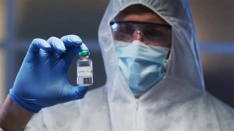 Caucasian Male Medical Worker Wearing Protective Clothing Mask And Gloves Holding Vaccine Vial