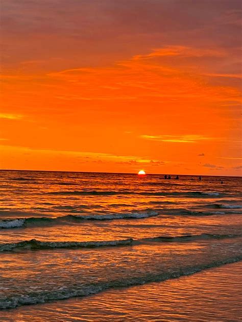 A View Of The Sunset At The Shore From The Beach The Sky Is A Bright Orange With Half Of The