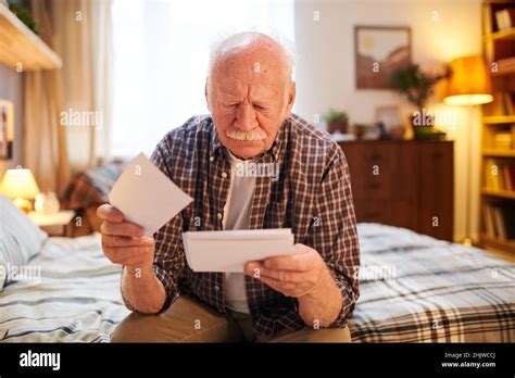 Old Man Sitting On The Bed In Bedroom And Looking At Photos In His