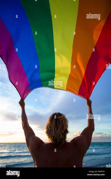 Man Holding A Fluttering Rainbow Gay Pride Flag On Beach At Sunrise Stock Photo Alamy