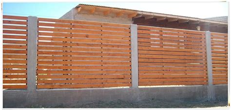 A Large Wooden Fence Next To A Building With Concrete Pillars And