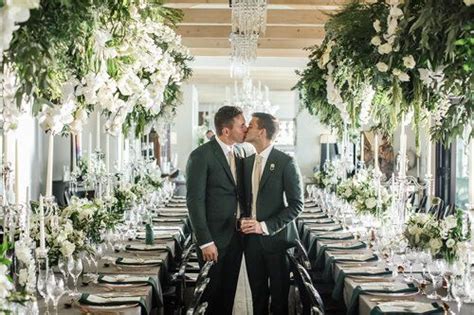 Two Men Kissing Each Other In Front Of Long Tables Covered With Flowers