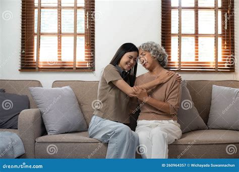 Loving Adult Daughter Hugging Older Mother Standing Behind Couch At