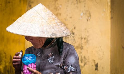 戴着圆锥形帽子和传统亚洲服饰的老可怜的女人拿着粉色和蓝色罐子的越南女士头饰下的皱纹脸站在亚洲越南黄高清图片下载 正版图片504811089 摄图网