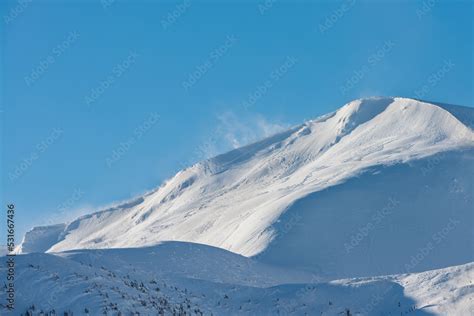 Snow-covered mountain top. The wind rises the snow on the mountain range. Stock Photo | Adobe Stock