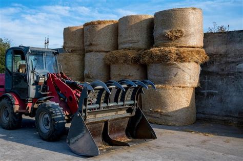 Premium Photo Farmer Unloading Round Bales Of Straw With A Front End