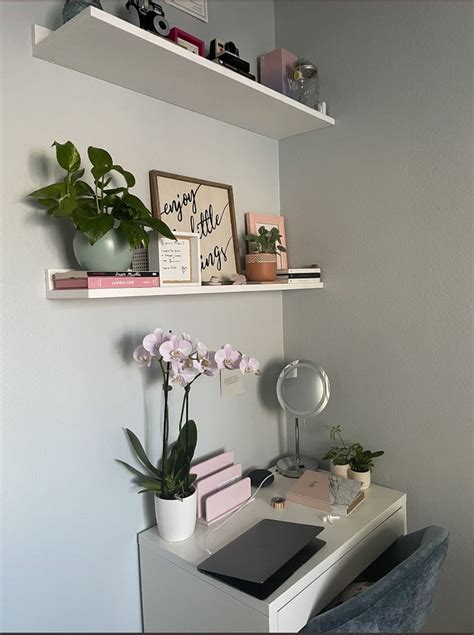 A White Desk Topped With Books And Flowers Next To A Wall Mounted Shelf