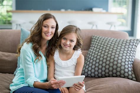 Smiling Mother And Daughter Sitting On Sofa Using Laptop In Living Room