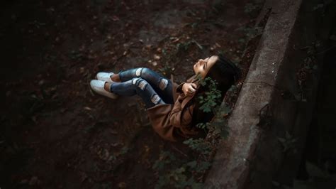 Sad Looking Girl Is Leaning Back On Wall Wearing Brown Shirt And Blue