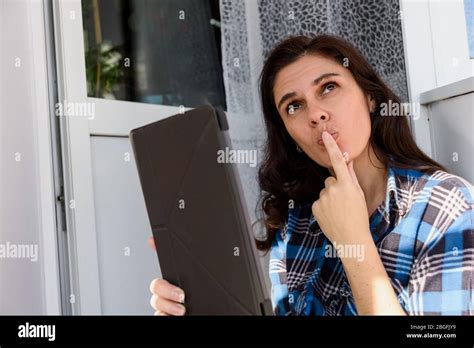 Brunette Girl Thinking And Holding Tablet Making A Selfie Or Video Call In Balcony By Touching