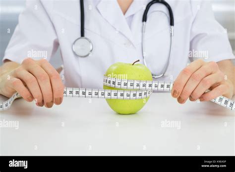 Close Up Of Dietician Measuring Green Apple With Measuring Tape Stock