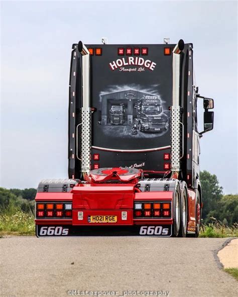 A Red Semi Truck Driving Down A Road Next To Tall Grass And Trees In