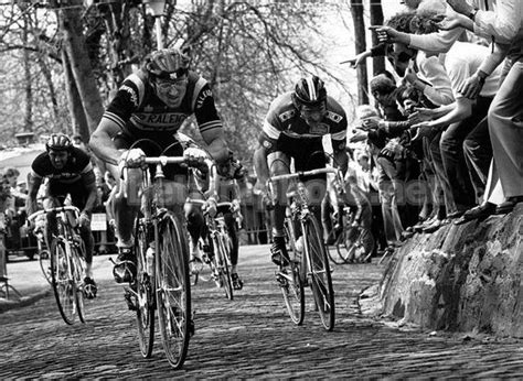 Black And White Photograph Of Cyclists On Cobblestone Road With