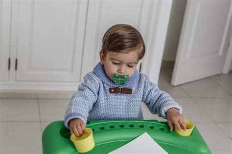 Een Weinig Blonde Jongen Met Een Fopspeen En Gekleed In Blauw Spelen Op Een Klein Bureau Stock
