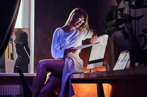 Une Femme Blonde Sexy Est Assise Sur La Table Tout En Lisant Des Documents Importants Photo