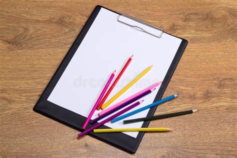 Colorful Drawing Pencils And Clipboard With Blank Paper On Wooden Table