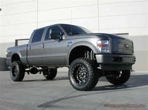 A Large Silver Truck Parked In Front Of A White Building With Black