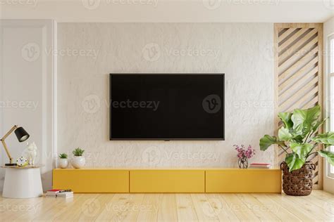 On a plaster wall background, a TV is mounted on a yellow cabinet in a ...