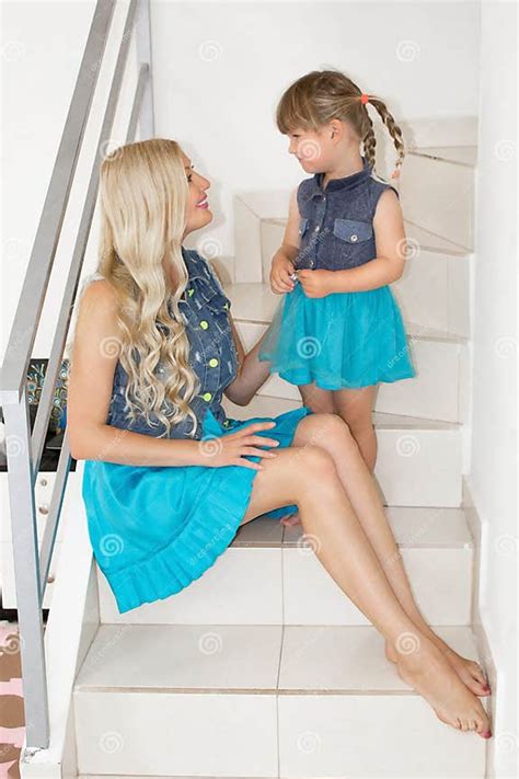 Mom And Daughter In Identical Dresses Are Sitting On The Stairs