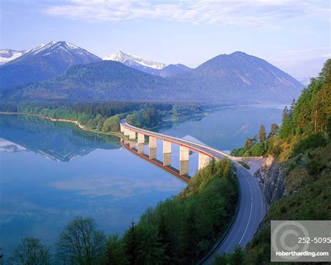 Reflections Of A Road Bridge Over Lake Sylvenstein With Mountains In