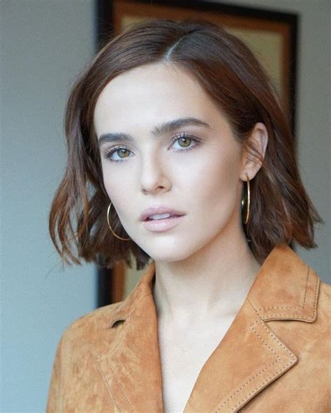 A Woman With Short Hair Wearing A Tan Jacket And Gold Hoop Earrings On