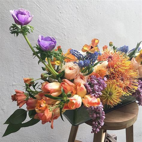 An Arrangement Of Flowers On A Stool In Front Of A White Wall With