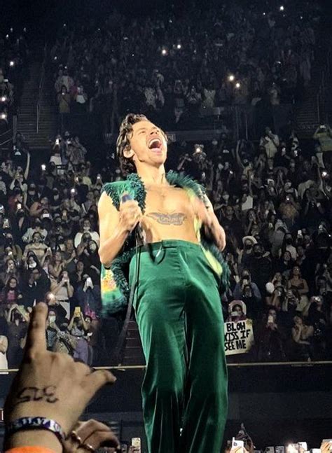 A Man In Green Pants Singing Into A Microphone While People Watch From