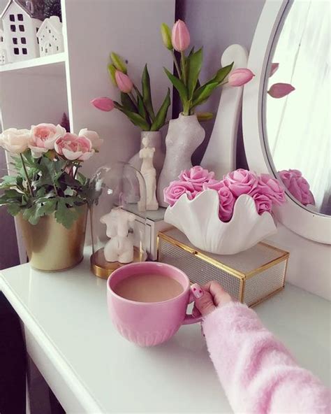 A Person Is Holding A Cup In Front Of A Dresser With Flowers And Other