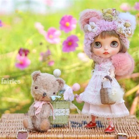 A Doll And Teddy Bear Sitting On A Wicker Basket With Flowers In The