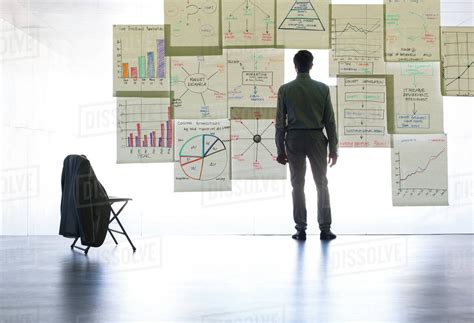 Businessman Looking At Graphs And Charts On Glass Wall In Office