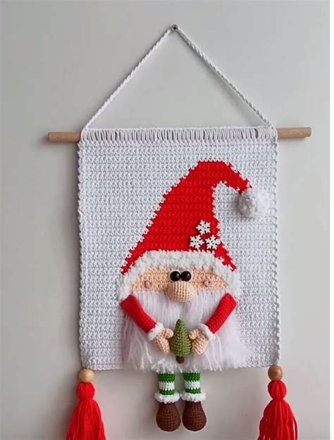 A Crocheted Santa Clause Hanging On A Wall With Tassels And Decorations