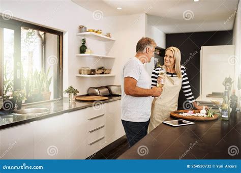 Mature Couple Cooking Drinking Wine And Preparing A Meal Together While Bonding Having Fun And