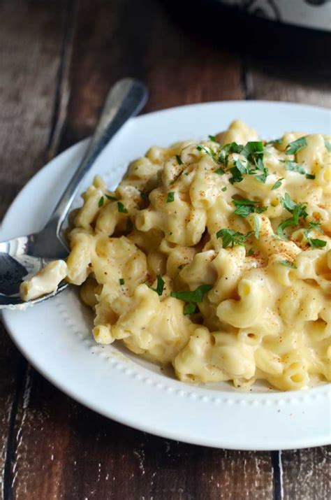 A White Plate Topped With Macaroni And Cheese Covered In Parsley Next