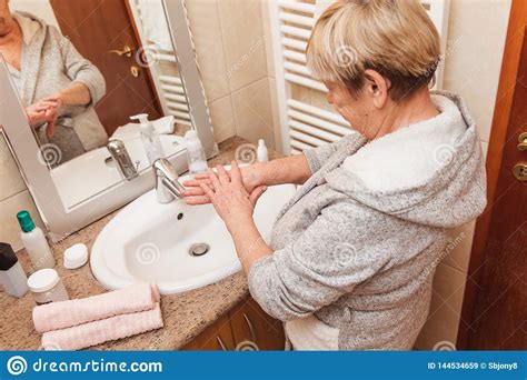 Senior Woman Touching Her Soft Face Skin Looking In Mirror At Home