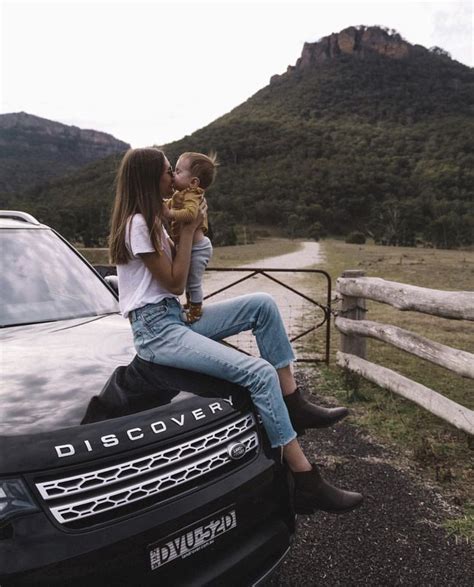 A Woman Is Sitting On The Hood Of A Car While Holding A Baby And