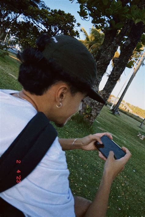 A Person Sitting In The Grass With A Cell Phone And Looking At