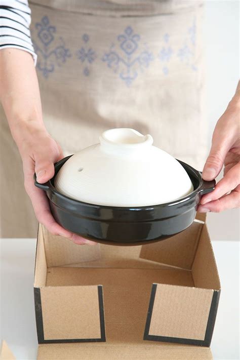 A Person Is Holding A Black And White Pot In A Box