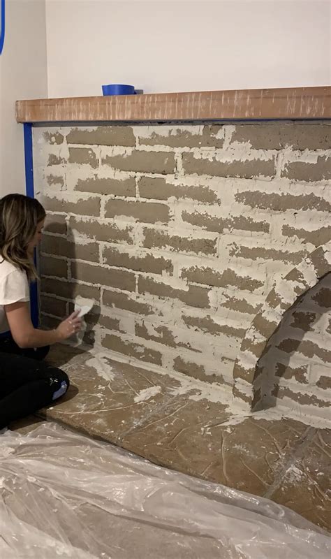 A Woman Sitting On The Ground Painting A Brick Wall With White Paint