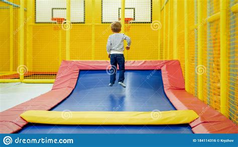 Rear View Photo Of Little Boy Jumping And Having Fun On Trampoline At