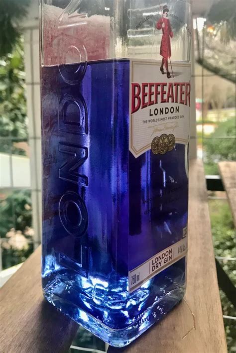 A Bottle Of Beefeater London Gin On A Wooden Table With Trees In The