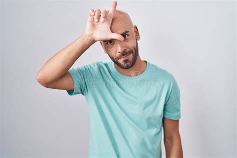 Middle Age Bald Man Standing Over White Background Making Fun Of People With Fingers On Forehead