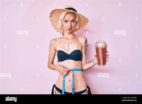 Junge blonde Frau mit Tattoo trägt Bikini mit Maßband und trinken Smoothie ahnungslos und
