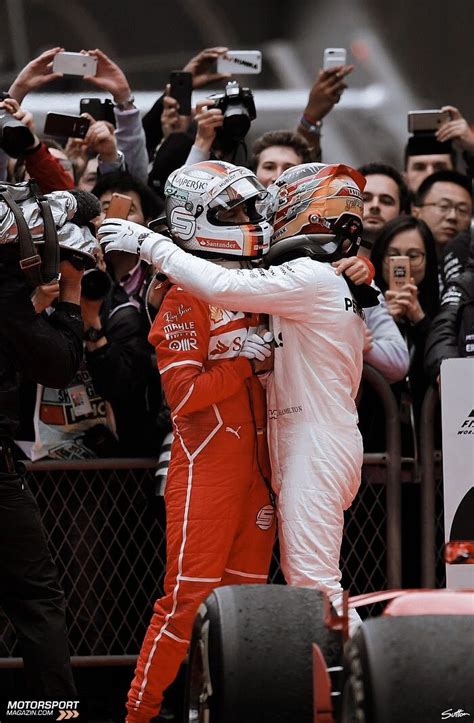 Two Men Hugging Each Other On Top Of A Race Track With People Taking