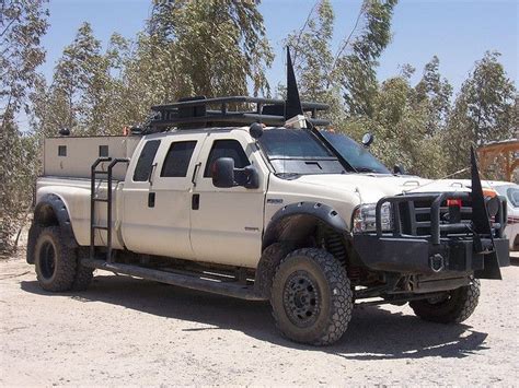 a large white truck parked on top of a dirt field next to trees and bushes