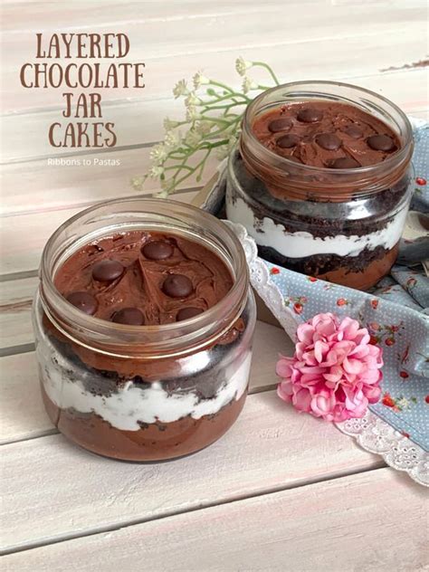 Two Mason Jars Filled With Layered Chocolate Jar Cakes On Top Of A Table Next To Flowers