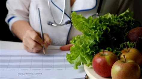 Nutritionist Woman Writing Diet Plan On Table Full Of Fruits And