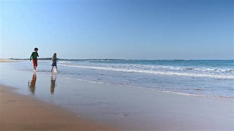 Caucasian beautiful kids walking together barefoot and playing on the empty sandy beach, smiling ...