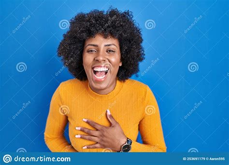 Black Woman With Curly Hair Standing Over Blue Background Smiling And Laughing Hard Out Loud