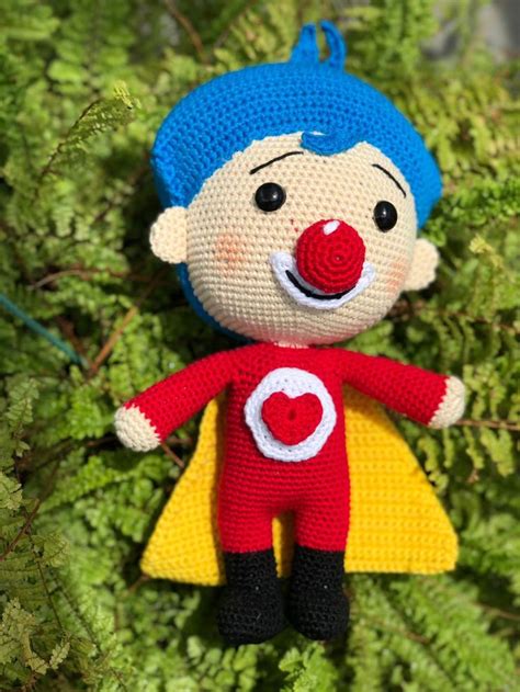 A Crocheted Clown Ornament Hanging On A Tree Branch With Green Leaves